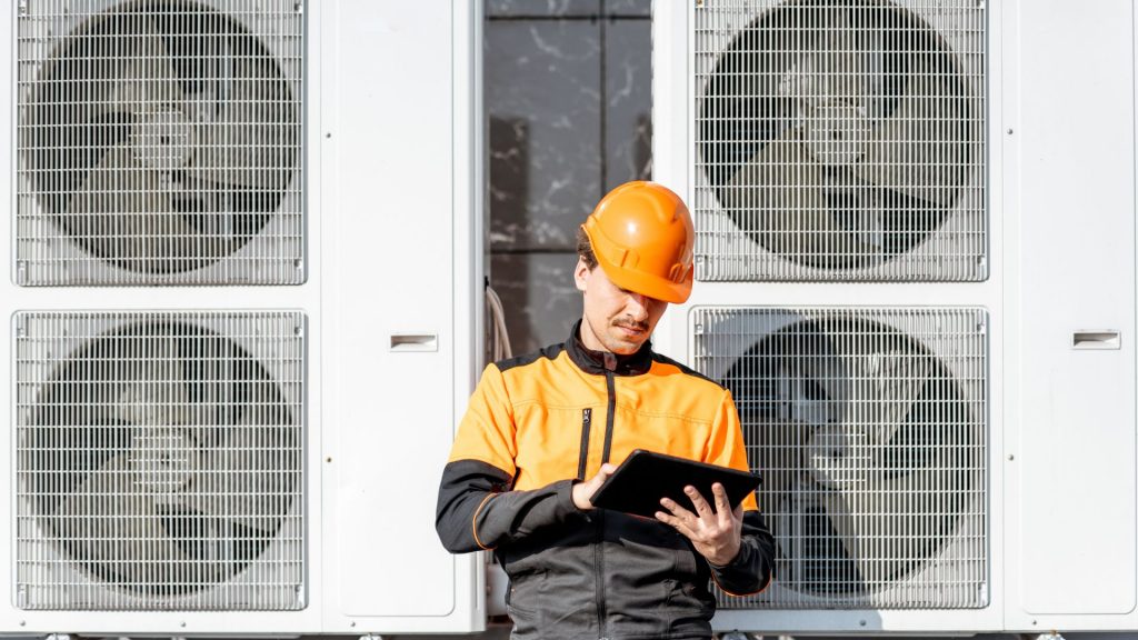 A technician is holding a tablet in front of an air conditioning system